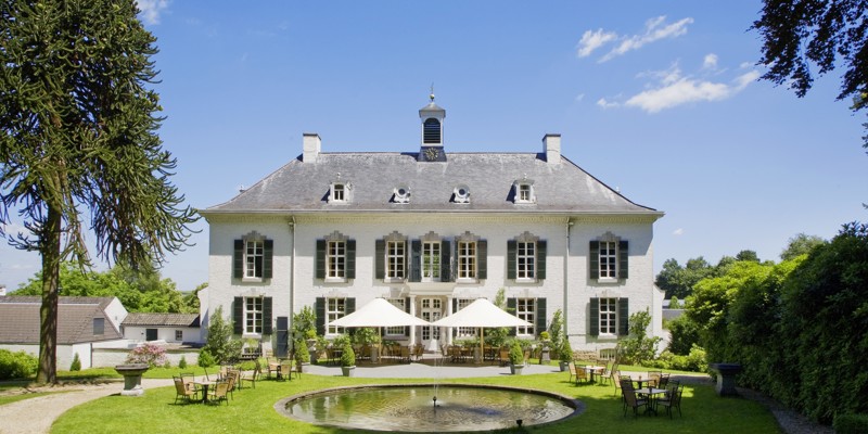 Chique wit hotel met een tuin ervoor incl. terras, grasveld en ronde vijver. 