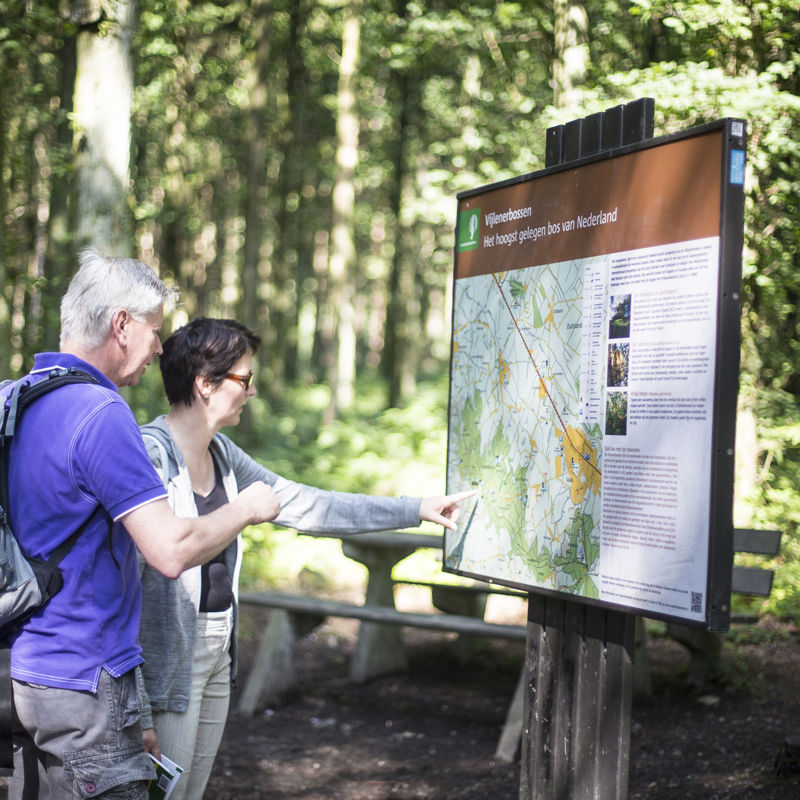 Twee wandelaars kijken op een infobord voor wandelroutes in het Vijlenerbos