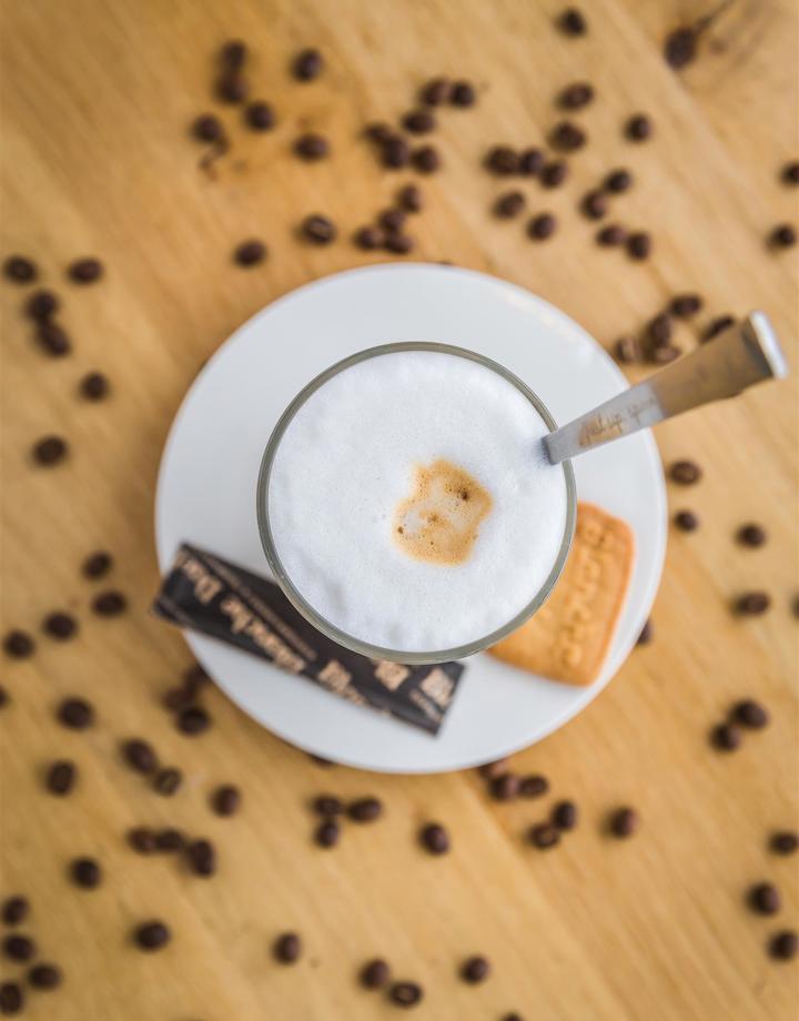 Een vers kopje koffie op een schoteltje met een koekje en suiker gezien van boven omringd met koffiebonen op een houten tafel